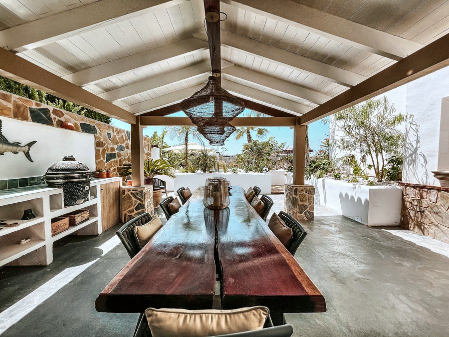 De lange eettafel onder de overkapping, met houtgestookte kamado en marlin aan de muur