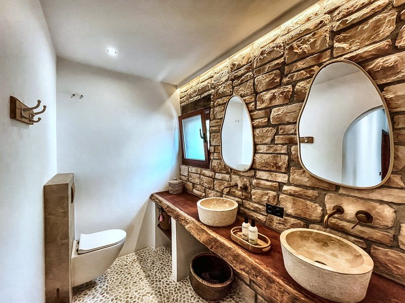 De badkamer met natuurstenen wand en dubbele spiegels